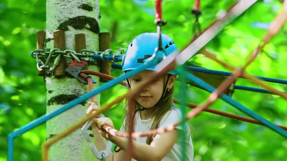 Extreme Rope Adventure in the Park - a Little Girl in Helmet Moving Over the Rope Bridge on High