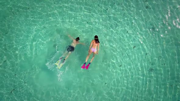 Aerial view of man and woman swimming in masks and flippers in turquoise water.