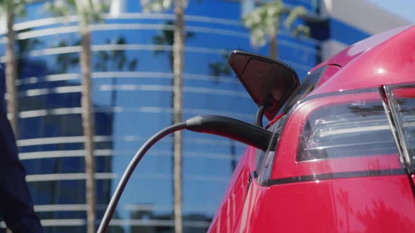 Closeup Caucasian Adult Man in Blue Suit Pulls Out Charging Cord at Red Vehicle