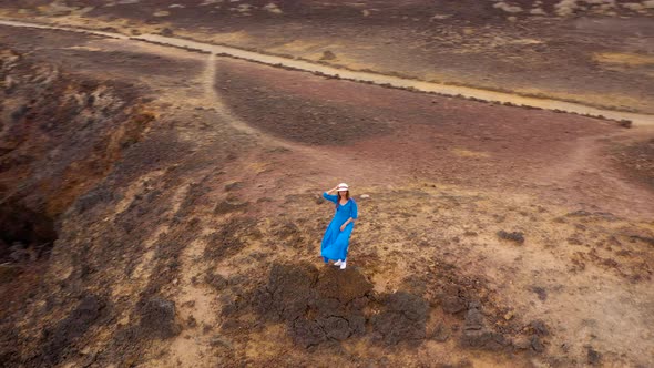 Aerial View of Woman in a Beautiful Blue Dress and Hat Stands on Top of a Mountain in a Conservation