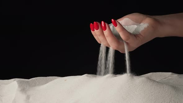 Woman with Handful of White Dry Sand in Her Hands Spilling Sand Through Her Fingers on Black Studio