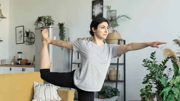 A Young Girl Does A Muscle Stretching Exercise, Stands on One Leg in a Yoga Pose, Is At Home