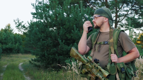 Man In Camouflage With Guns. Speaking On The Radio