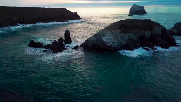 Flying between huge ocean rocks close to crashing waves into the setting sun at Sand Dollar Beach in