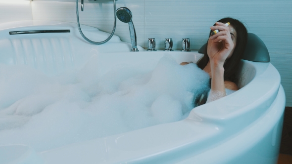 Girl Take Bath Full Of Foam In Bathroom. Smoke Electronic Cigarette. Resting