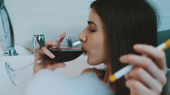 Girl Take Bath Full Of Foam. Smoke Electronic Cigarette, Drink Red Wine.