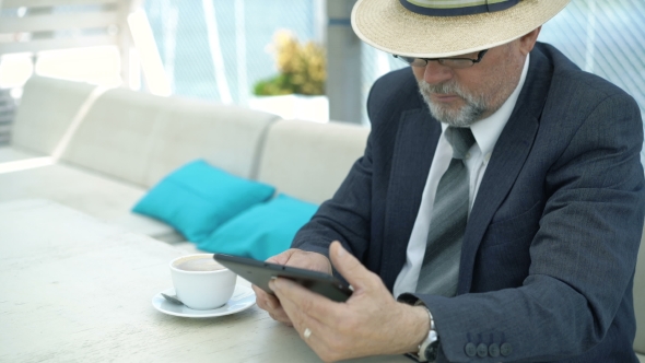 Old Businessman Using Tablet And Drinking Coffee In Cafe. 