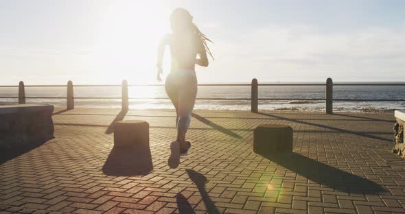 African american woman running on promenade by the sea at sundown