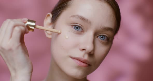 A Young Woman Applying Foundation with a Dropper to Her Cheeks Closeup