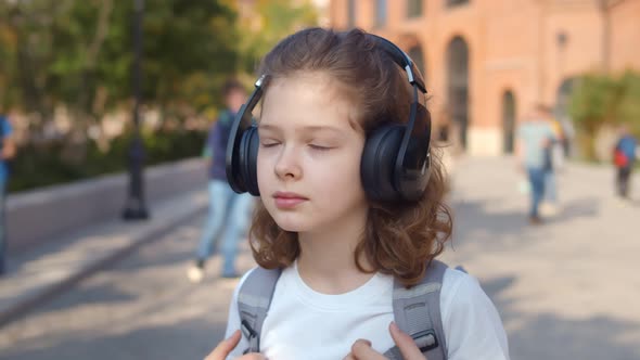 Portrait of Schoolgirl with Backpack in Headphones Listening To Music Outdoors