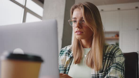 Young Focused Woman Freelancer Wearing Eyeglasses Working Online at Home Typing on Laptop and