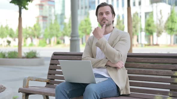 Thinking Young Man Using Laptop While Sitting on Bench