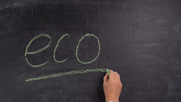 A man's hand writes the phrase ECO on a chalkboard in green chalk