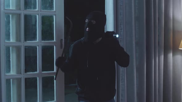 Thief Man Holding Flashlight And Using Crowbar Open The Door Before Entering Someone's House