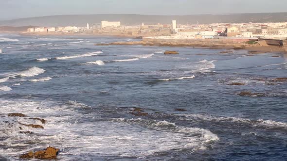 Panning to the right from Atlantic ocean with rollers coming in to the walls of Essaouira, Morocco.