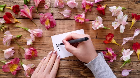 Writing MOM by hand on a card near flowers top view