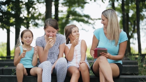 Attractive Mom With Three Daughters In a Park. Woman Enjoys The Tablet.