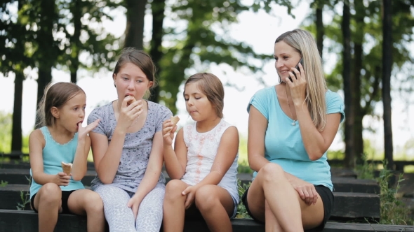 Mother Talking On The Mobile Phone While Sitting Next To The Kids In The Park.