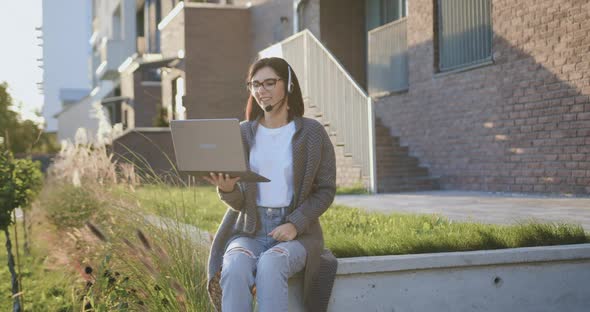 Good-looking Woman Using Computer Laptop with Headset Talking on Video Call Looking at Camera