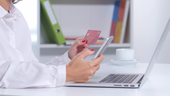 Girl Makes a Purchase Online Using Phone And Laptop In The Office. 