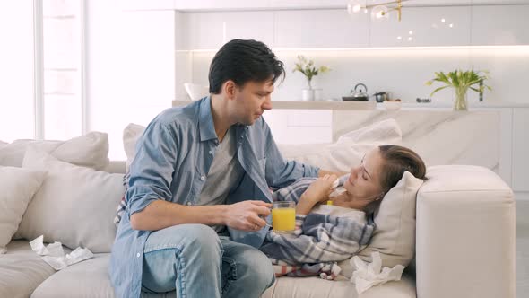 Man Approaches Woman Lying on Sofa She Is Wrapped in Blanket and Feels Bad