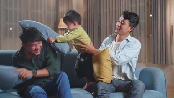 Happy Asian Gay Couple Having Fun With Their Lovely Son Fighting Pillows In Living Room