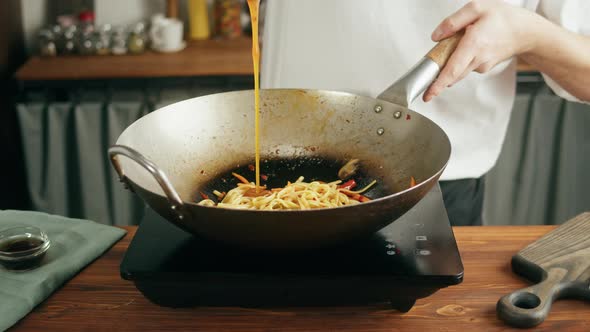 Chef Cooking Asian Rice Noodles with Fried Meat and Spicy Vegetables in Wok Pan