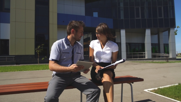 Businesswoman And Businessman Sitting On a Bench And Discussing The Business Plan