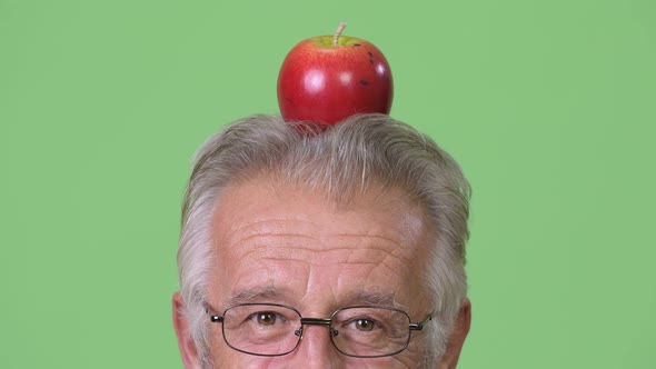 Head Shot of Senior Man with Apple on Top of Head Against Green Background