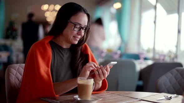 Middleaged Woman is Drinking Coffee in Restaurant in Daytime Sending Message By App in Smartphone