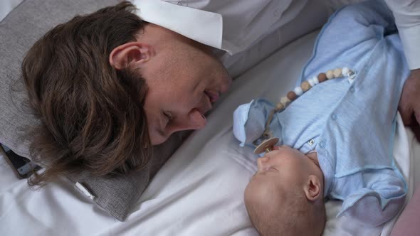 Top View Happy Father Singing Lullaby Lying with Newborn Baby Son on Soft Cozy Bed at Home
