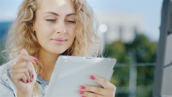 Portrait of  Attractive Young Woman Uses Tablet on a Summer Area in the Cafe.