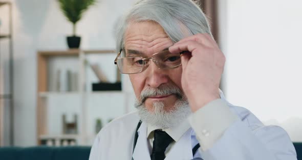 Doctor Putting on His Eyeglasses and Looking Into Camera with Trustful Face Expression Indoors