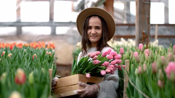 A Young Farmer Girl in a Hat Holds a Box with Bouquets of Tulips in Her Hands