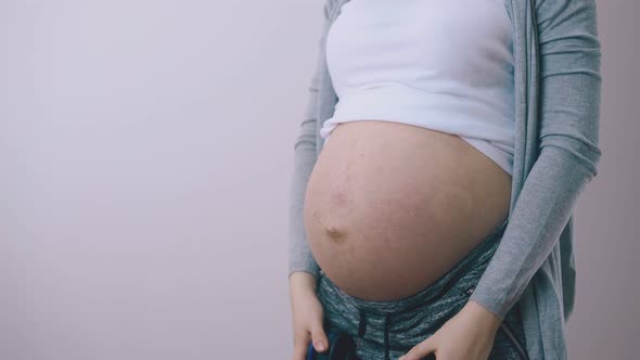 Young Pregnant Lady Puts Headphones on Belly Near Wall