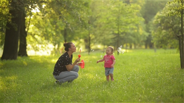 Mother and Girl Blowing Soap Bubbles Outdoor. Parent and Kid Having Fun in Park.