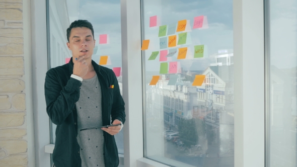 Young Handsome Man Writing On Sticky Notes On Panoramic Window In Modern Office