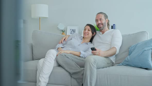Caucasian loving man and woman couple sit on sofa watch movie on TV together in living room at home.
