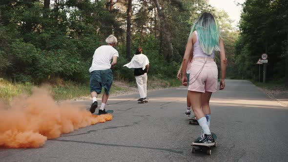 Rear View of a Group of Young People Boys and Girls Skate Through the Park with a Smoke Bomb