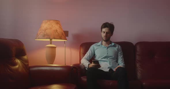Guy looks at the smartphone sitting on the red sofa at home