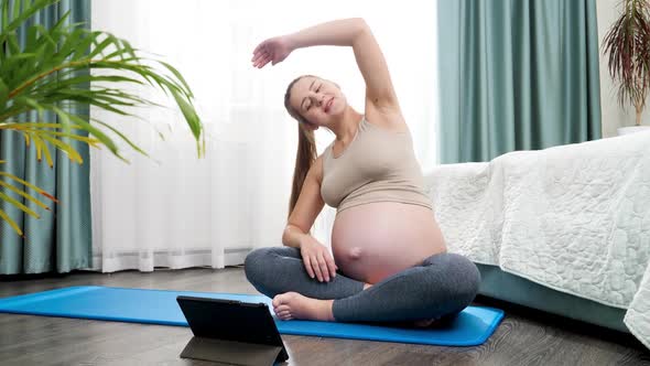 Smiling Pregnant Woman Practicing Yoga Online Looking on Tablet Computer