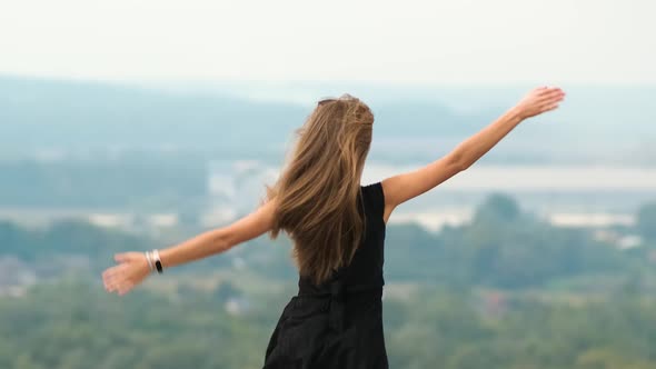 Back View of a Young Energetic Woman with Long Hair in Short Summer Dress Dancing Happily in Nature