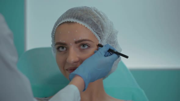 The Beautician in the Office Marks the Client's Face with a Pencil Closeup