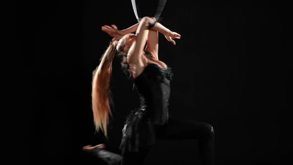 Slim Young Woman Performing Trick Hanging on Air Hoop Spinning in Slow Motion at Black Background