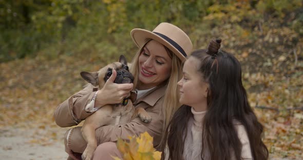 Stylish Mother and Daughter Playing with Pet Sitting in Autumn Park