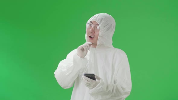 Asian Man Wear Protective Uniform Ppe And Use Mobile Phone Then Thinking In The Green Screen Studio