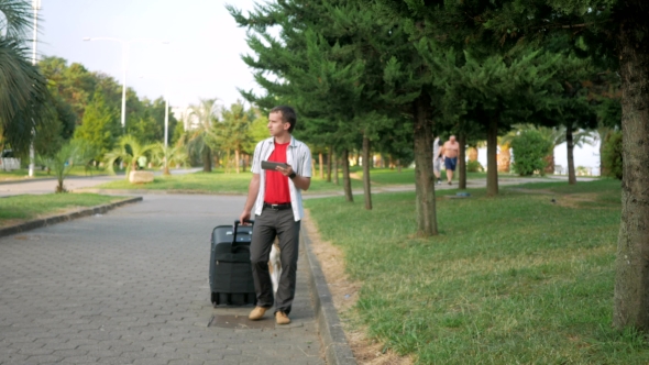Young Man Tourist Is With a Large Suitcase On Wheels Around The City Park