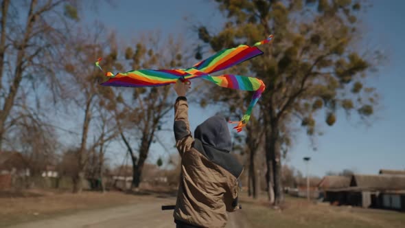 A Happy Boy with a Flying Rainbow Kite Rides a Bicycle on the Road