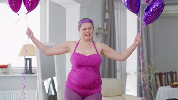 Medium Shot of Funny Obese Woman Raising Balloons Imitating Weight Lifting Looking at Camera