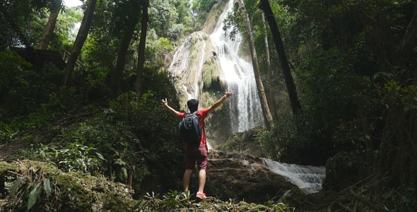 Man Standing in Front of Waterfall With His Hands Raised